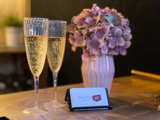 Zwei Sektgläser neben einer Vase mit lila Blumen und einer Visitenkarte.