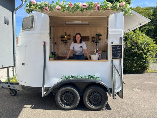 Ein mobiler Verkaufsstand mit blühenden Pflanzen und einer Verkäuferin darin.