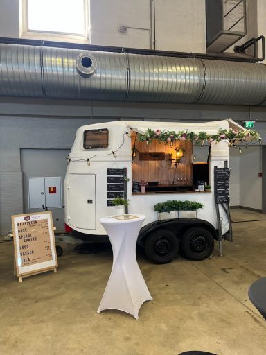 Mobiler Verkaufswagen mit Stehtisch und Menütafel in einer hellen Halle.